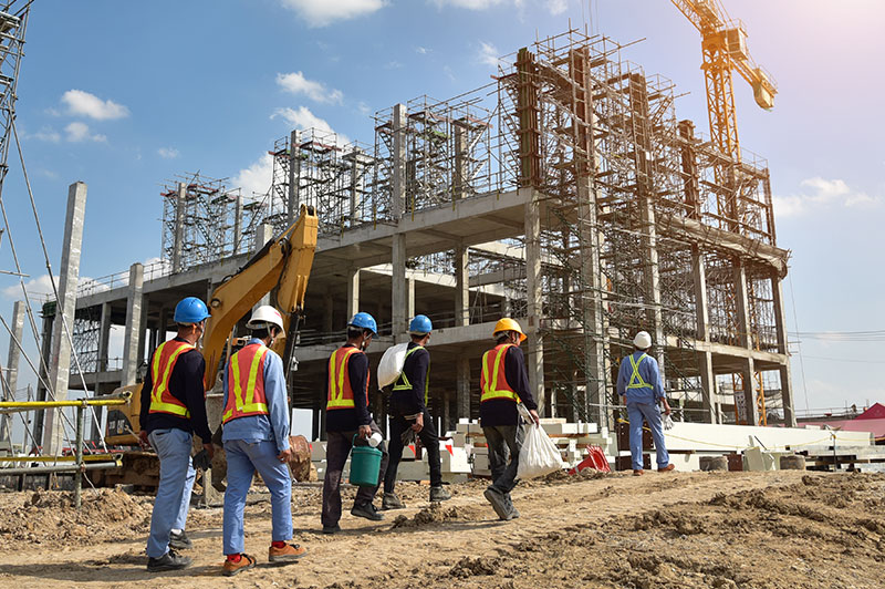 Advanced Building Corporation crew members on an active commercial construction site in Wisconsin, with multi-story structural framing, scaffolding, and heavy equipment in the background.